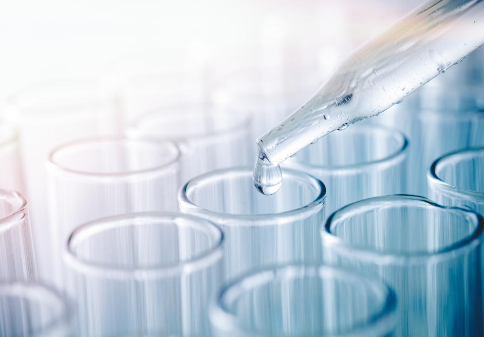 Pipette dropping liquid into a single test tube on a rack of many.