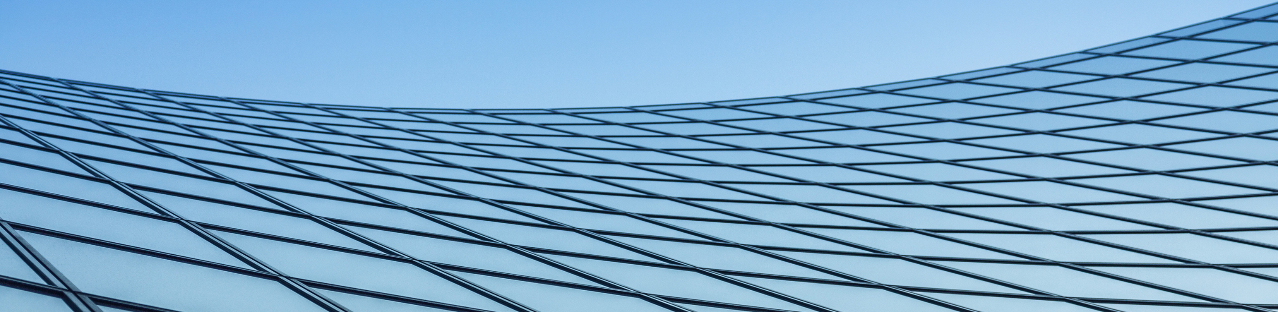 A modern glass facade with a grid pattern reflecting the clear blue sky, creating a sleek and dynamic architectural effect. Image selected for Company Overview webpage.