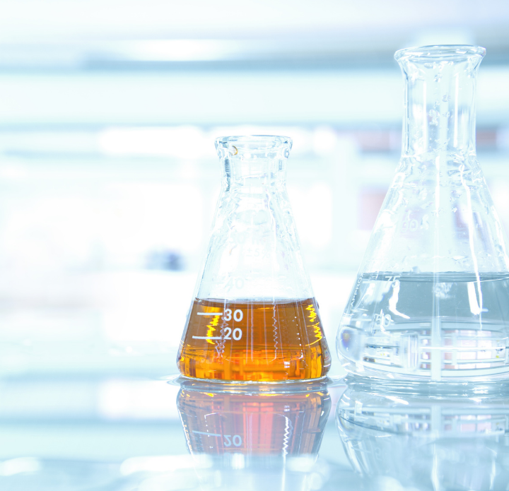 Two conical flasks on a reflective surface in a lab; one with amber liquid, the other with clear fluid. Bright laboratory environment for WPPO testing.