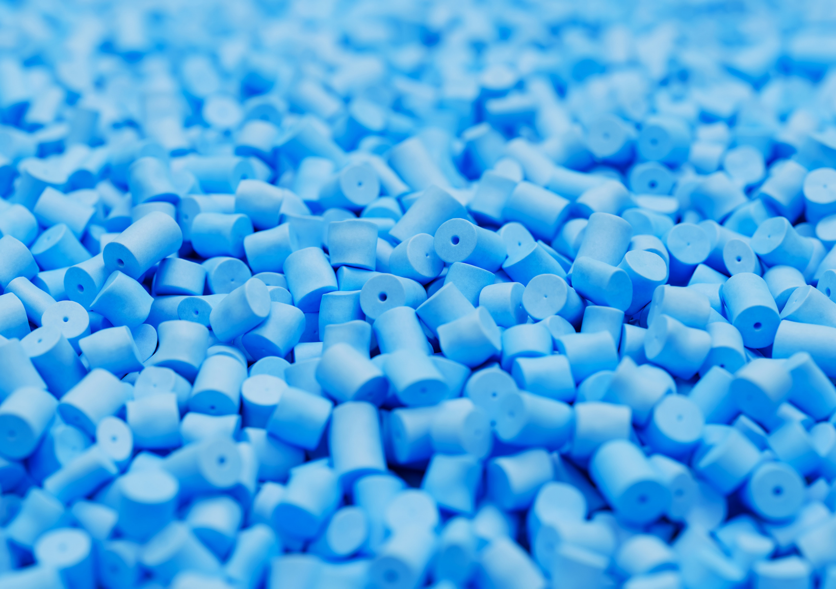Close-up of numerous small blue plastic pellets, cylindrical in shape, creating a textured surface. The image conveys a sense of industrial production and waste plastic pyrolysis oil (WPPO).