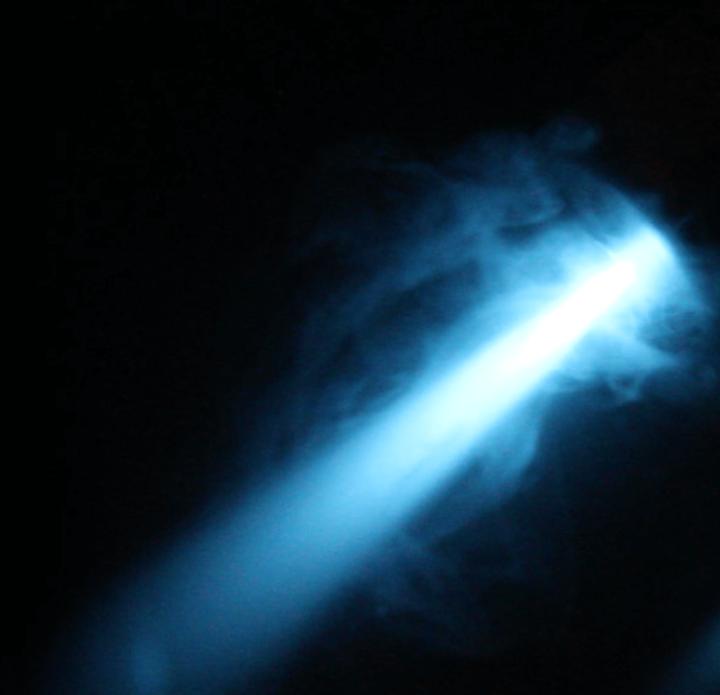 A beam of bright blue light pierces through dark smoke, creating a mysterious and ethereal atmosphere against a black background.