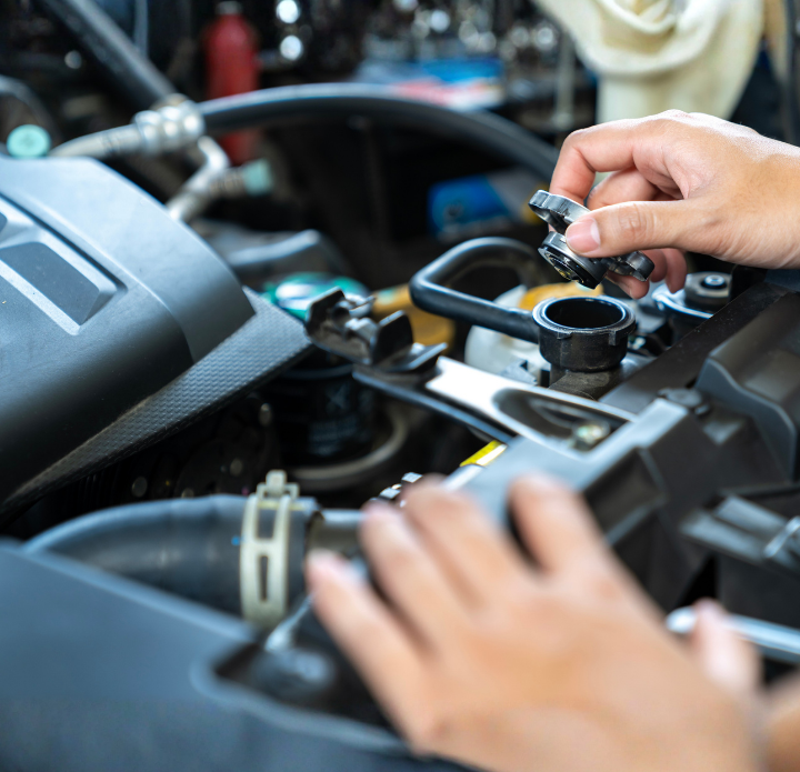 Hands opening the radiator cap of a car engine. The focus is on the hands and engine, conveying a sense of maintenance and mechanical care.