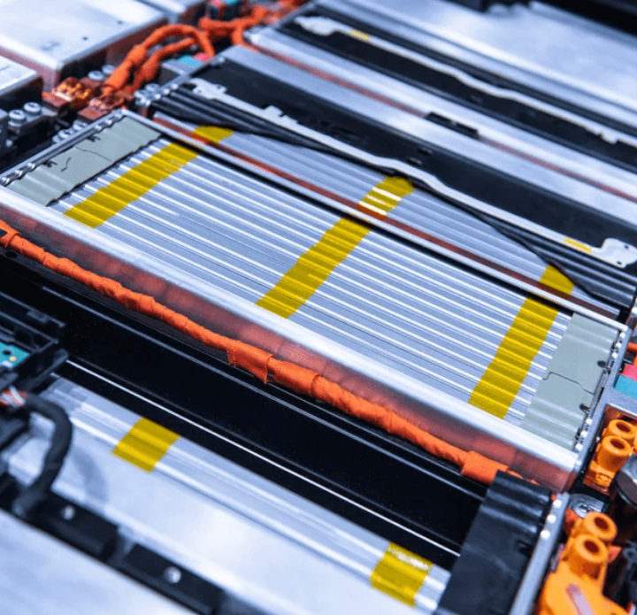 Close-up of an electric vehicle battery pack with multiple aligned silver cells, orange cabling, and connectors, highlighting advanced technology.