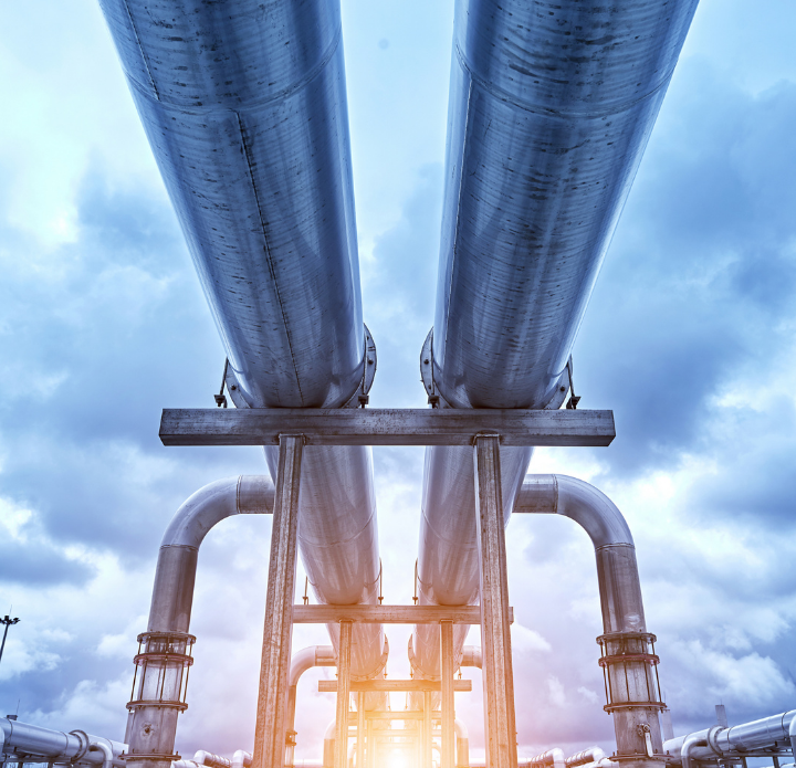 Two large parallel industrial pipelines stretch into the distance against a cloudy sky. Sunlight glows beneath, creating a dramatic and imposing scene. PAC Powered by Emcee.