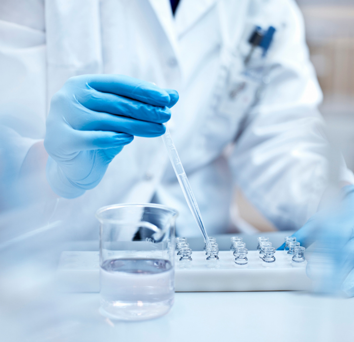 A scientist in a lab coat and blue gloves uses a pipette to transfer liquid into test tubes. The scene is bright and focused, conveying precision. PAC Powered by Emcee.