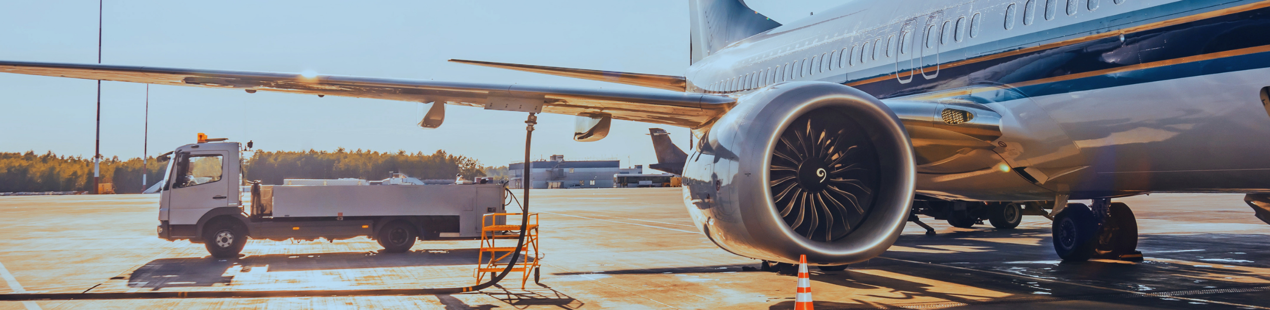 A commercial airplane on a sunny tarmac, with its jet engine in focus. A service vehicle is parked nearby, conveying a sense of routine airport operations. PAC Powered by Emcee.