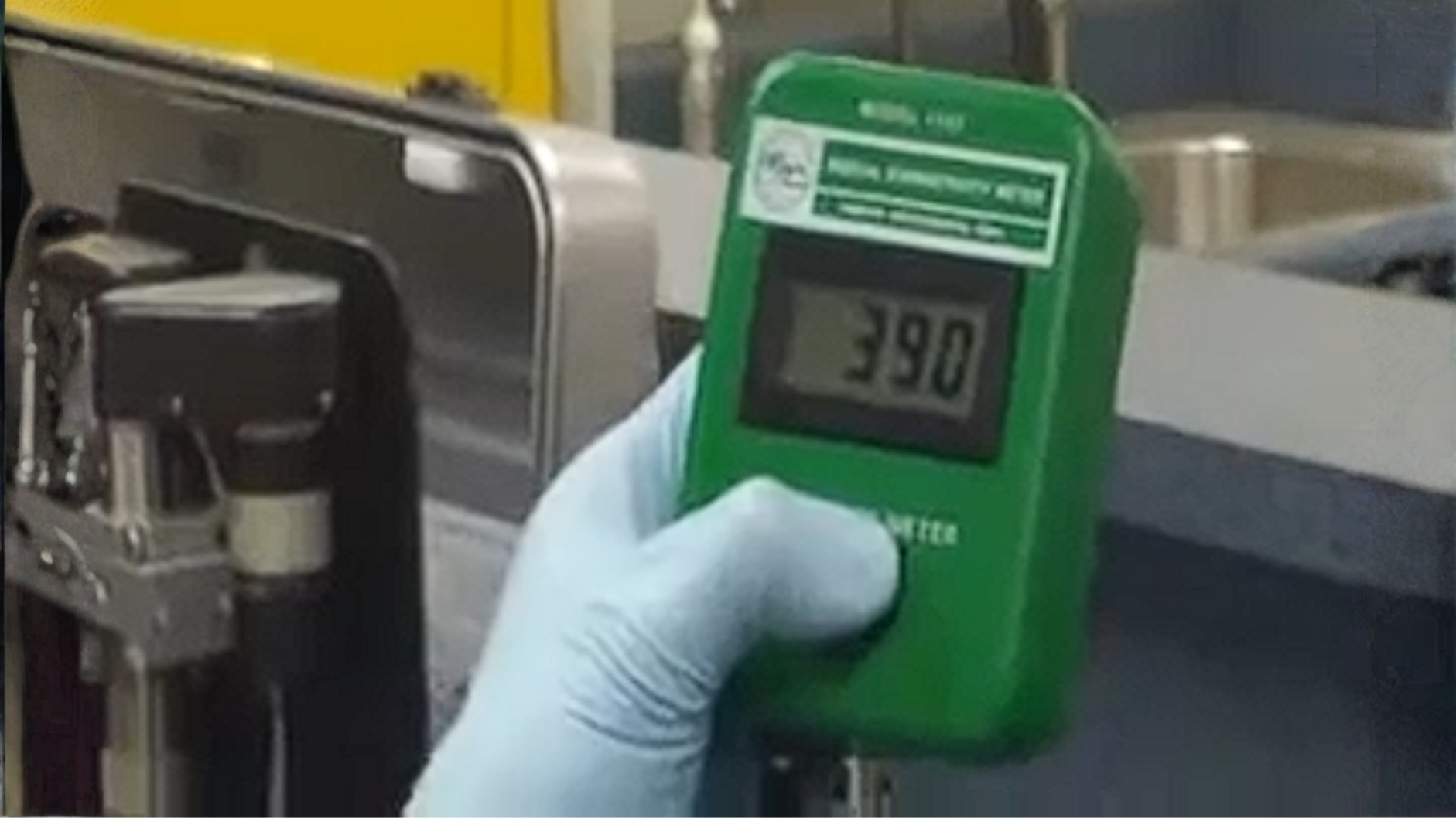 A gloved hand holds a green PAC Powered by Emcee Model 1152 digital conductivity meter displaying 
