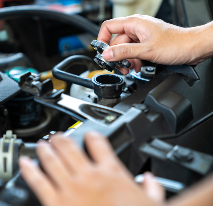 A hand unscrewing a car's radiator cap under the hood, showing various engine components in close-up. The scene conveys maintenance and care.