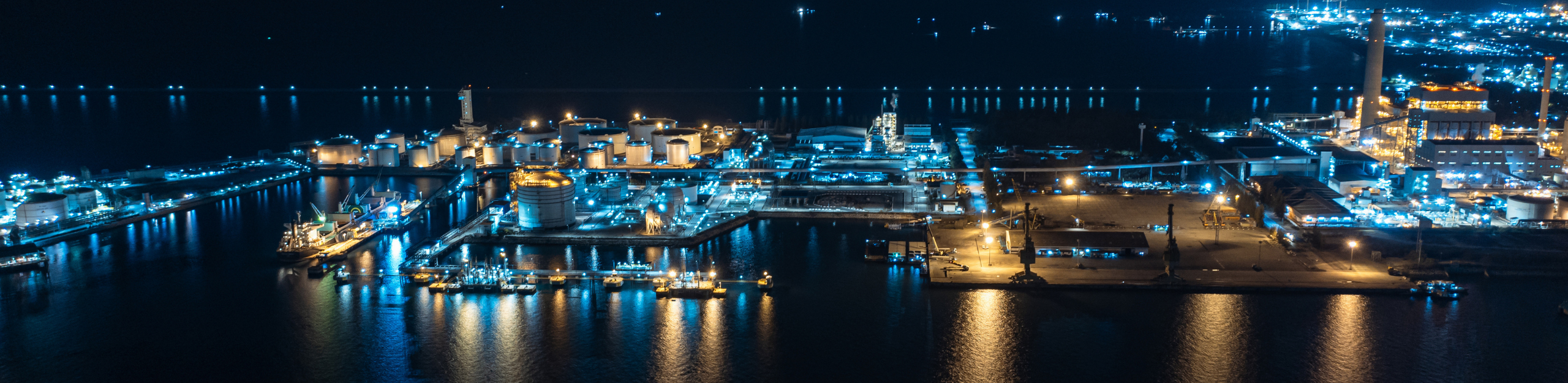 Nighttime aerial perspective of a sprawling LNG value chain industrial complex, with lights highlighting various structures and facilities.
