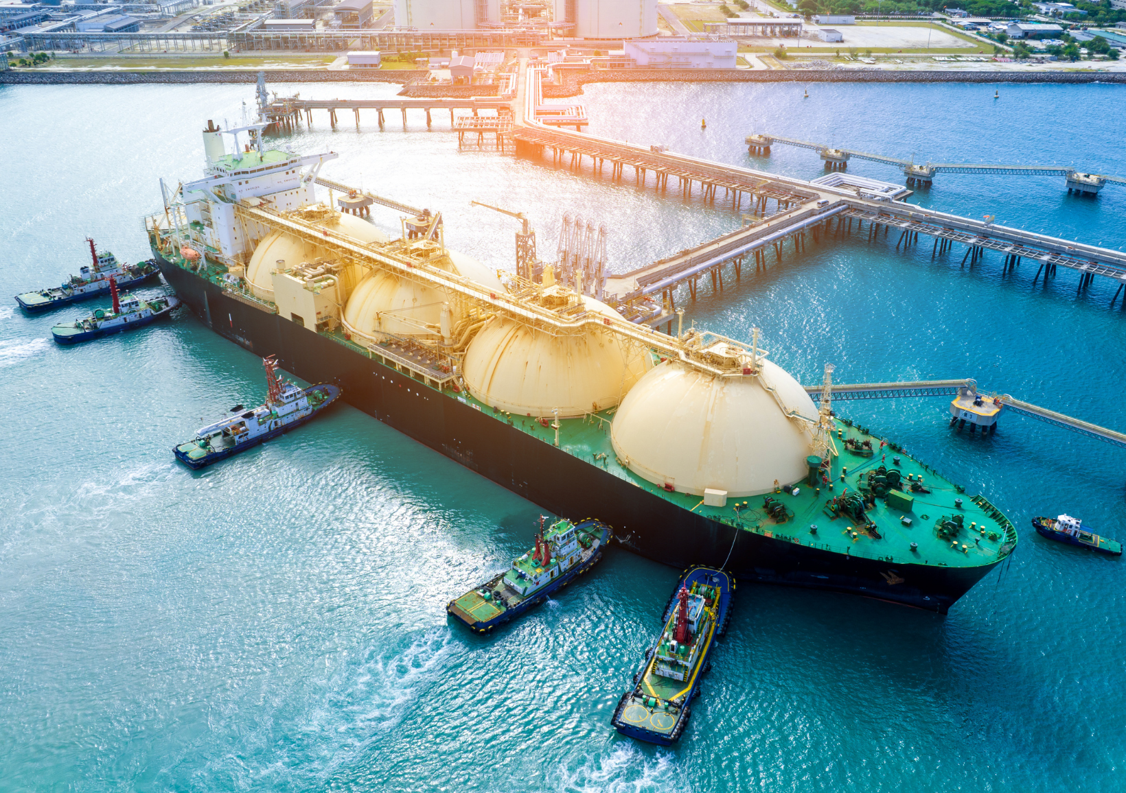 An LNG value chain tanker anchored in the water near a dock, with clear skies and calm waves surrounding it. LNG Analysis.