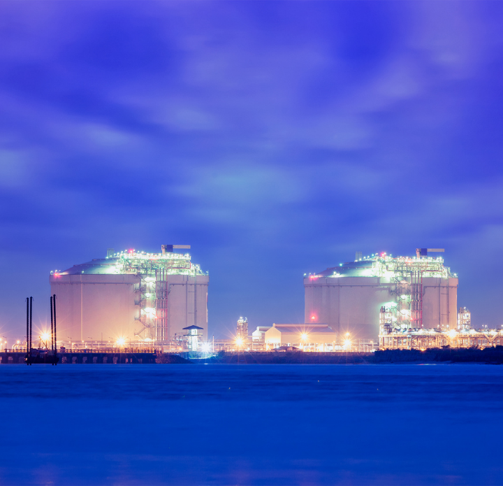 Two large oil refineries illuminated at night, showcasing numerous lights against a dark sky.