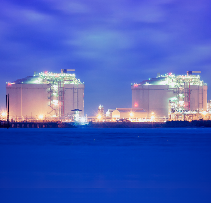 Two large oil refineries illuminated at night, showcasing numerous lights against a dark sky. LNG Analysis.