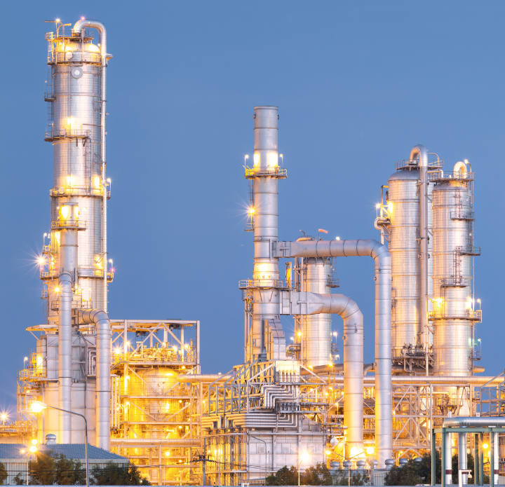 A large industrial refinery with towering smokestacks and complex machinery against a clear blue sky.
