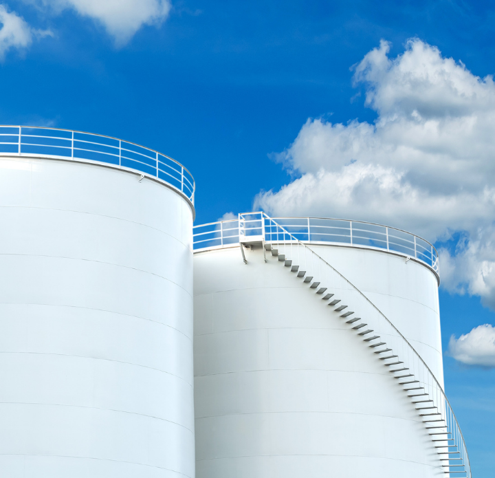 Two large white LNG tanks with a ladder on top, positioned side by side in an industrial setting. LNG Analysis.